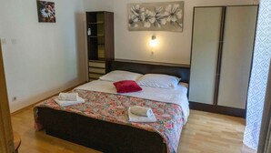 A neatly made bed with a floral bedspread, a red pillow, and two towels on the side. - Holiday apartment with air conditioning (Jurandvor)
