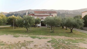 A two-story house with a red-tiled roof, surrounded by olive trees and a grassy area. - Holiday apartment with air conditioning (Jurandvor)