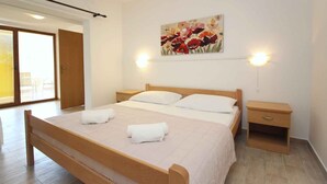 Un dormitorio con cama de madera, dos mesitas de noche, un cuadro en la pared y un ventanal corredero que da a un balcón.