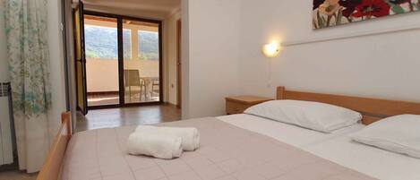 A bedroom with a bed, a nightstand, a painting, and a view through a sliding door to an outdoor area.