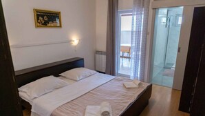 Ett hotellrum med en säng, ett nattduksbord, en väggmonterad lampa, en inramad tavla och utsikt över en balkong och en glasdörr som leder ut.