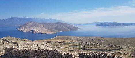 Un paisaje costero con una vista despejada de una masa de agua extensa, terreno rocoso y una estructura de piedra en primer plano.