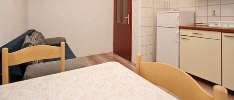 Een kleine, compacte kamer met een bed, een tafel, een stoel, een bank, een televisie en een kitchenette met een koelkast en kastjes.