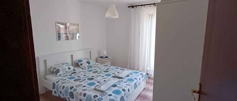 Un dormitorio con una cama, una mesita de noche, una lámpara y una ventana con cortinas.