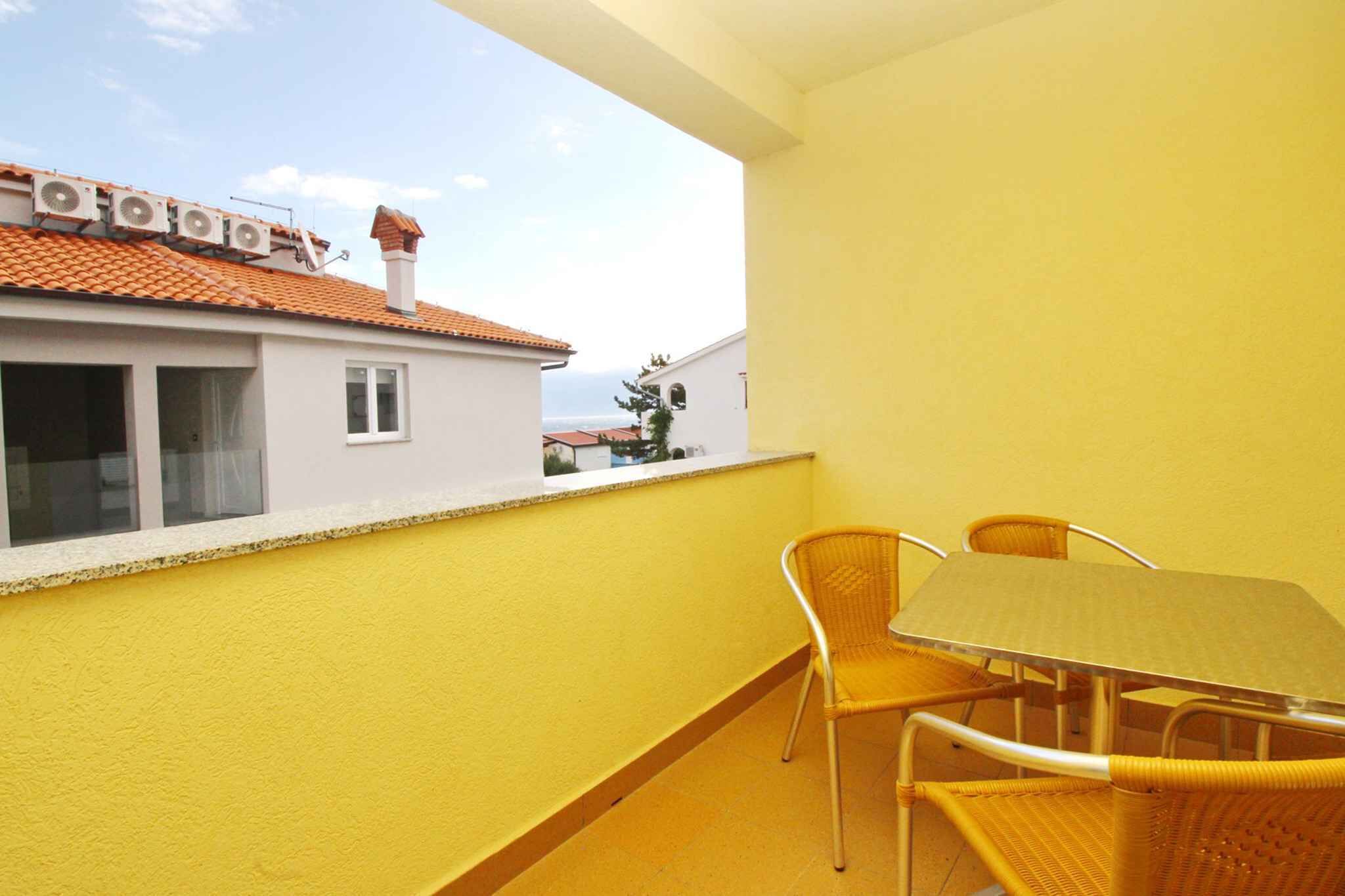 A balcony with yellow walls, a table, and two wicker chairs.