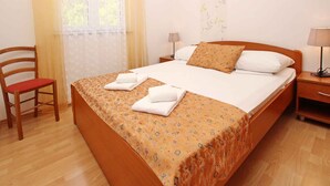 Una camera d'albergo con un letto grande, due comodini con lampade, una sedia di legno e una finestra con tende.
