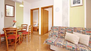 Un soggiorno con un divano decorato, sedie di legno, un tavolo da pranzo e una cucina visibile attraverso un'apertura.
