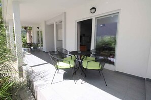 Une terrasse extérieure avec une table et des chaises, une porte-fenêtre coulissante et une vue sur la verdure.