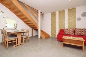 A living room with a wooden staircase, a dining area with chairs and a table, and a red sofa with patterned cushions. - Holiday flat with terrace near the beach (Baška)