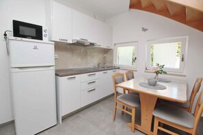 A modern kitchen with white cabinetry, a built-in microwave, and a dining area with a table and chairs.