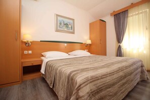 Une chambre d’hôtel avec un lit, deux lampes de chevet, un tableau au mur et une fenêtre avec des rideaux.