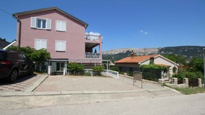 Ein pinkfarbenes, zweistöckiges Gebäude mit Balkon, ein Auto davor und ein Berg im Hintergrund.