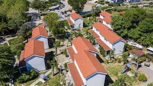 Ett bostadsområde med flera hus, alla med röda tegeltak och vita väggar. Man kan se infartsvägar och en lekplats med en rutschkana.