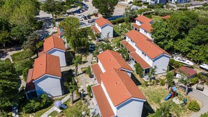 Una zona residenziale con diverse case, ciascuna con tetto in tegole rosse e pareti bianche. Si notano vialetti privati e un’area giochi con uno scivolo.