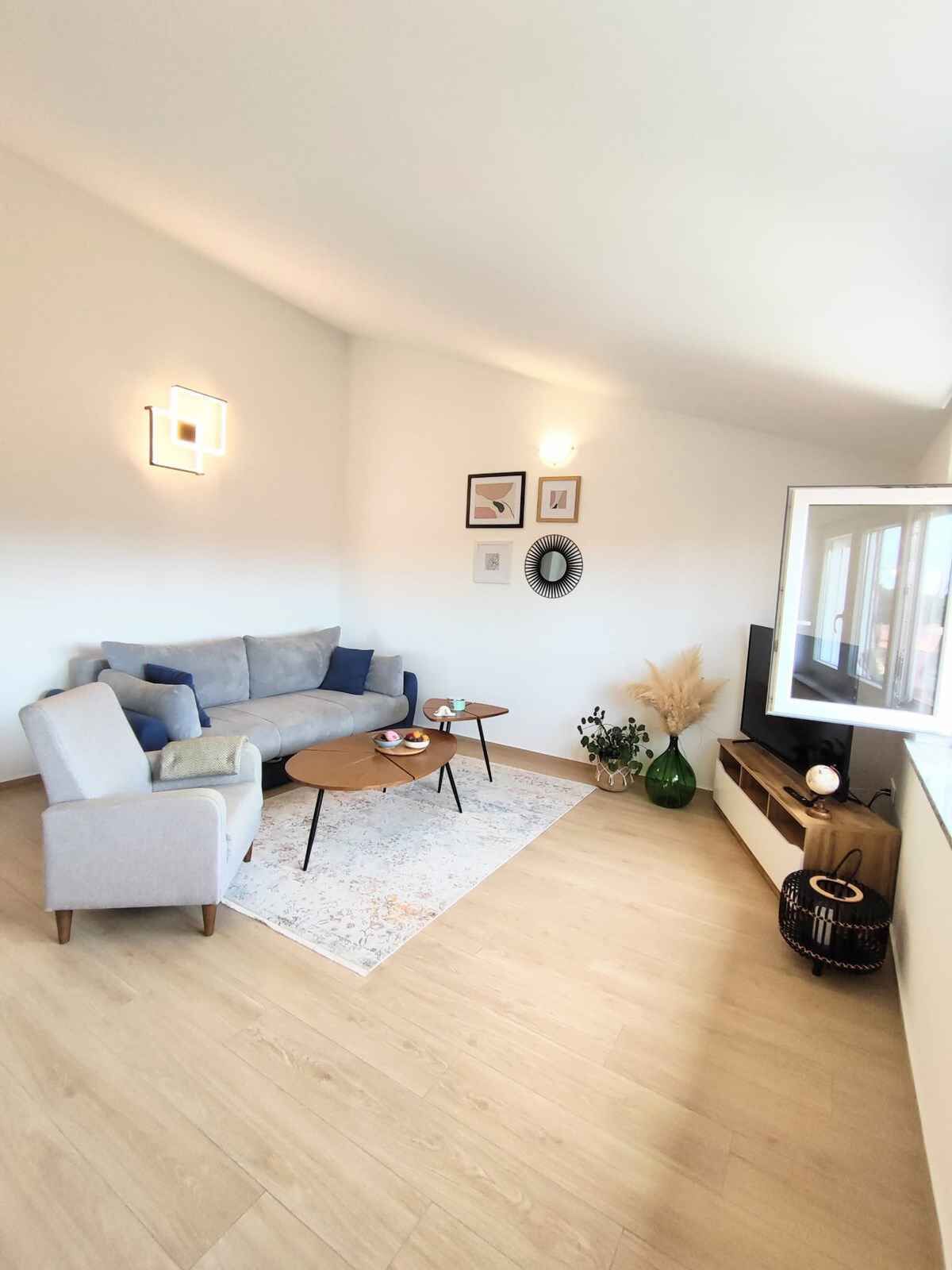 Uma sala de estar moderna com um sofá cinzento, uma mesa de centro e uma TV sobre um suporte de madeira.