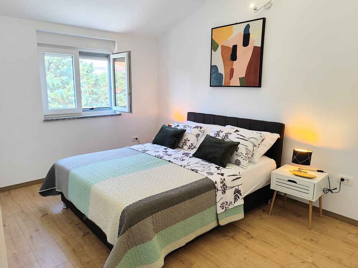 Een slaapkamer met een bed, nachtkastje, lamp en een raam.