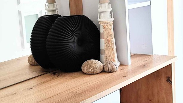 Ein Holzboden mit Dekorationen, darunter eine schwarze Vase, zwei kleine weiße Vasen und ein Leuchtturmmodell.