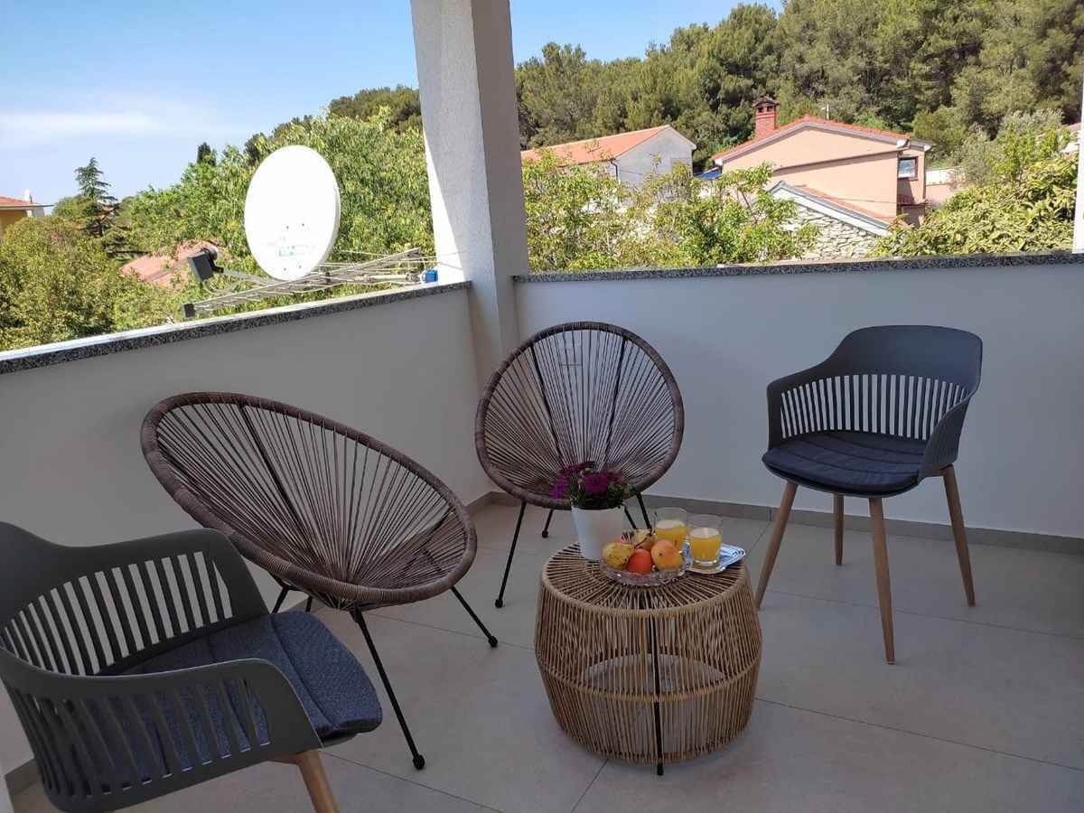 Varanda com cadeiras de vime, uma mesa pequena com frutas e bebidas, e uma antena parabólica.
