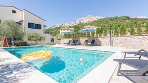 En swimmingpool med solstolar och parasoller, omgiven av en stenmur och med ett berg i bakgrunden.