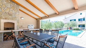 An outdoor patio with a stone fireplace, a pool, and a table with chairs. - Holiday apartment with shared-use pool (Jurandvor)