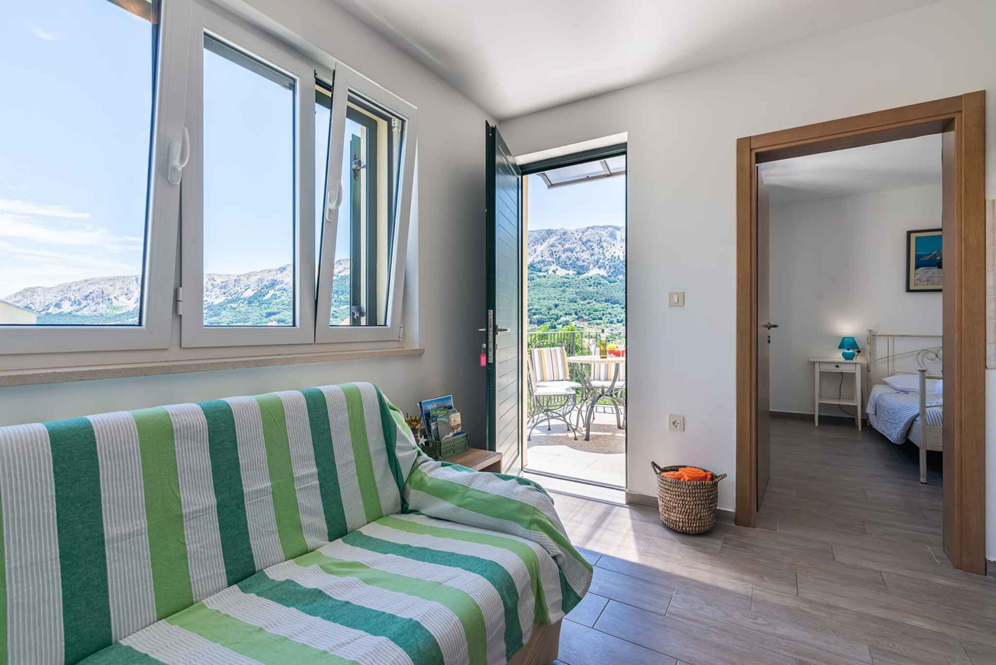 A room with a green-striped sofa, a sliding glass door leading to a balcony with a mountain view, and a small table with a lamp.