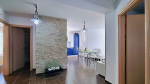 A modern kitchen with a stone accent wall, a dining area with a table and chairs, and a hallway with a wooden door and a ceiling light fixture. - Holiday apartment with terrace and private garden for exclusive use (Baška)