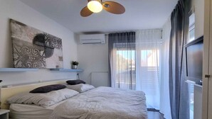 A bedroom with a bed, a ceiling fan, a wall-mounted air conditioner, and a window with curtains. - Holiday apartment with terrace and private garden for exclusive use (Baška)