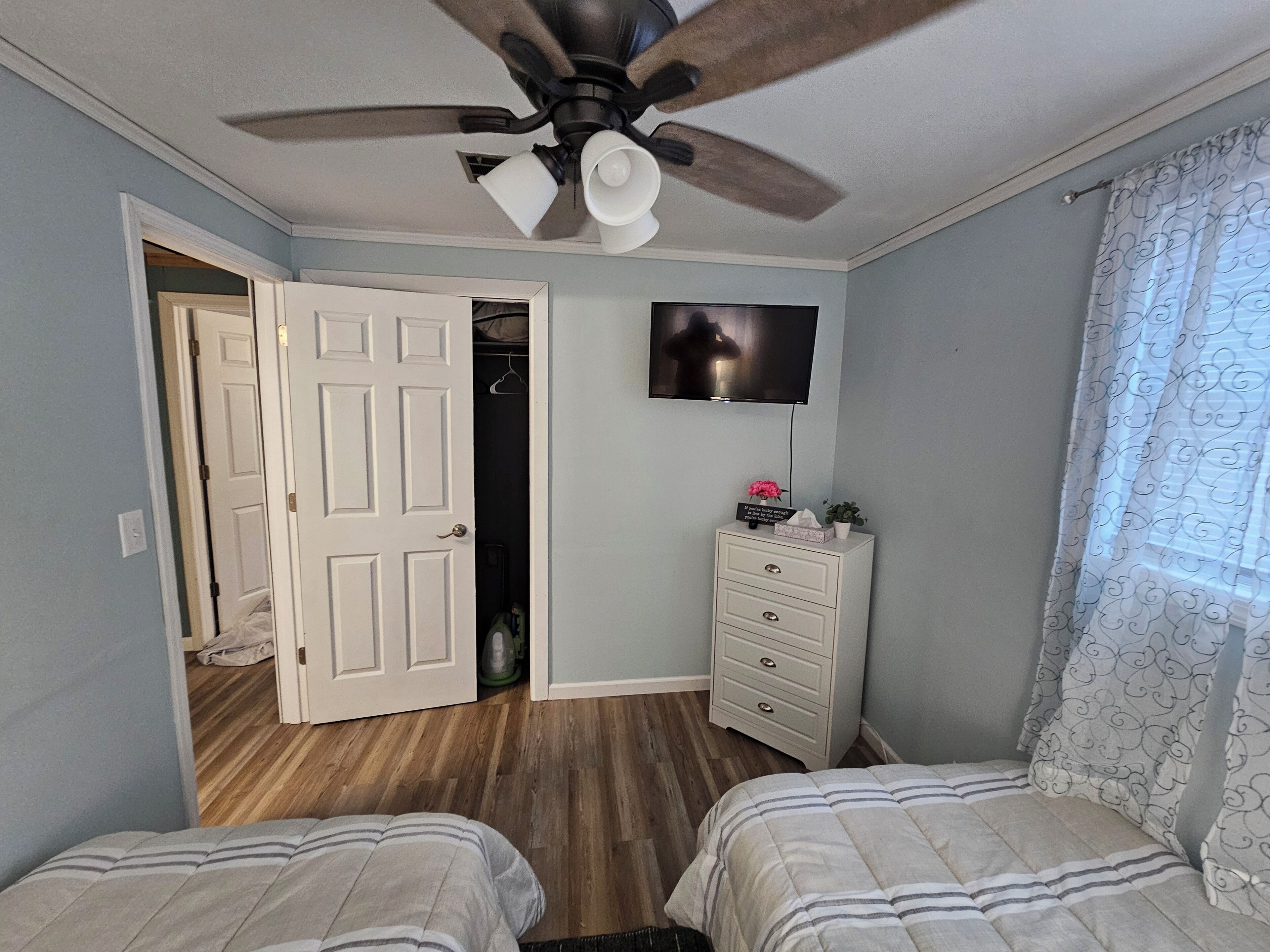Un dormitorio con dos camas, ventilador de techo, televisión, cómoda y armario.