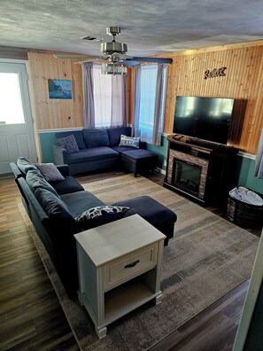 Ein Wohnzimmer mit Ecksofa, Fernseher und Kamin.