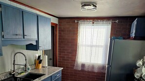 Una cocina con armarios azules, un lavamanos, un refrigerador y una ventana con cortina.