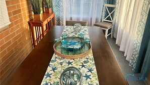 Un comedor con una mesa larga, cristalería decorativa y un camino de mesa estampado.