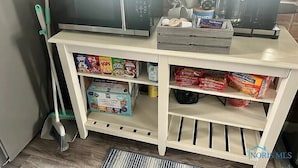 Una cocina equipada con microondas, cafetera y repisas repletas de aperitivos y café.