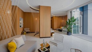 Eine moderne Hotelhalle mit einer Couch, Sesseln, einem Essbereich und einer großen Pflanze.
