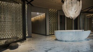 Ein modernes Badezimmer mit einer großen Marmorbadewanne, strukturierter Wandgestaltung und einer hängenden Leuchte.