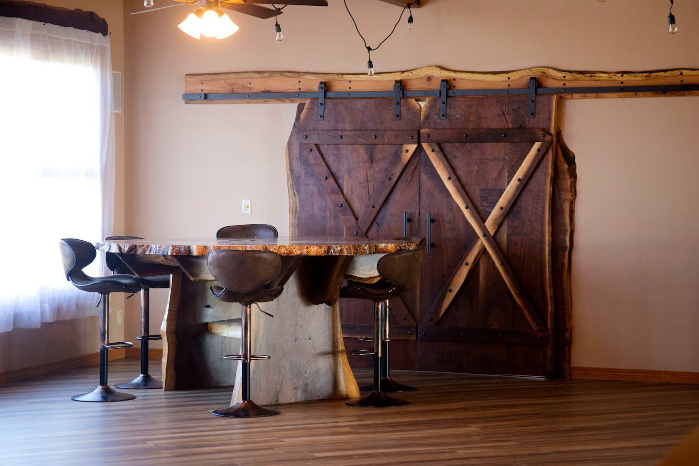 A dining area with a wooden table and chairs, a rustic barn door, and a hanging light fixture.
