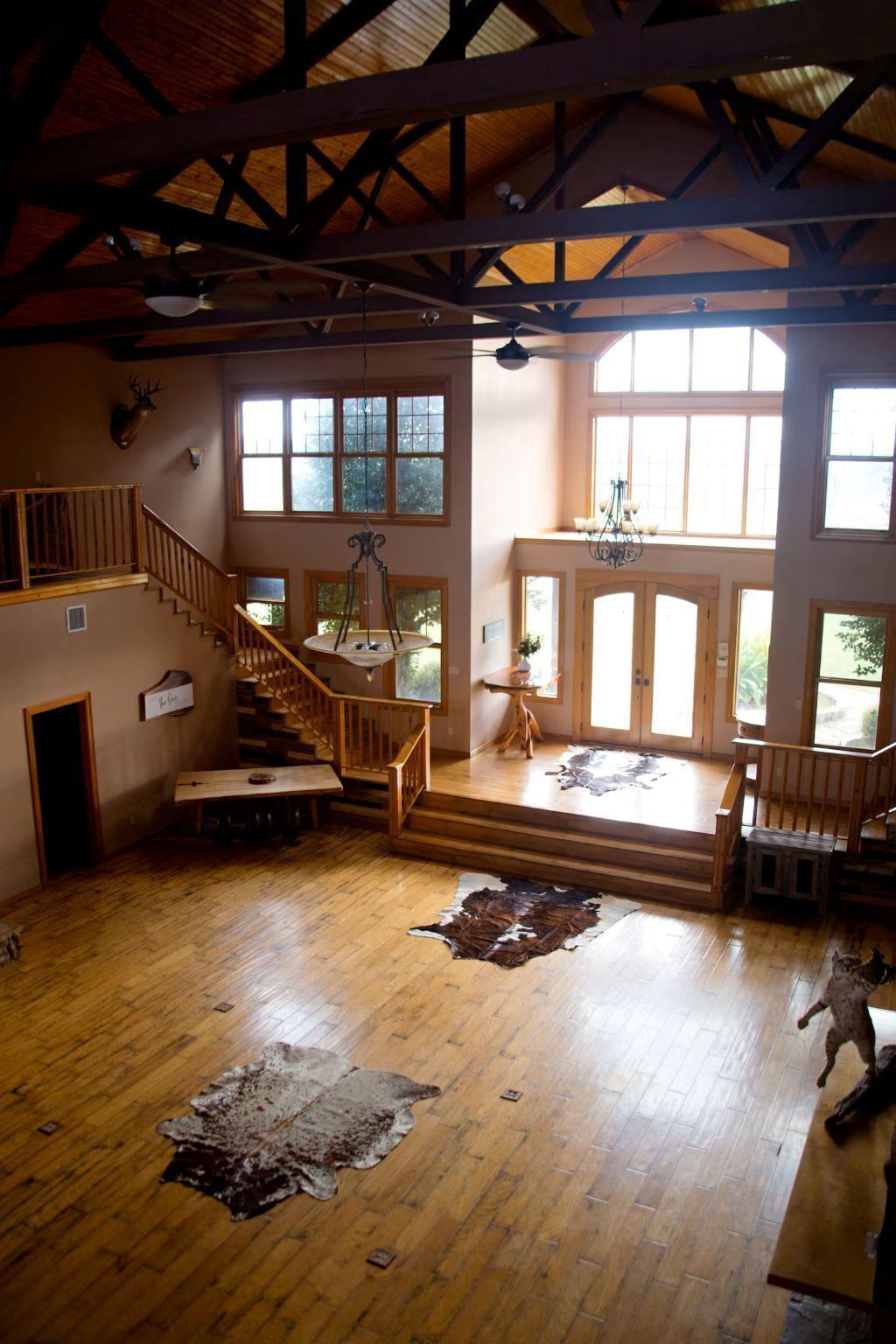 A spacious interior with a wooden staircase, a chandelier, and large windows.
