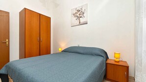 A bedroom with a bed, a wooden wardrobe, a bedside table with a lamp, and a wall-mounted painting. - Holiday apartment with air conditioning and balcony (Valbandon)
