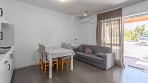 Ein modernes Wohnzimmer mit Esstisch und Stühlen, einem grauen Sofa und einem großen Fenster mit Vorhängen.