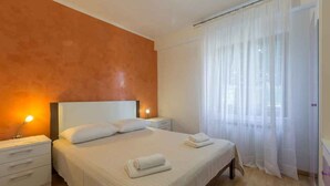 Ein Schlafzimmer mit Bett, weißen Vorhängen und einem Nachttisch mit Lampe.