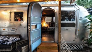 L'intérieur d'un wagon de train d'époque, avec un escalier en bois menant à un espace aménagé en chambre, une petite fenêtre et une porte en métal.