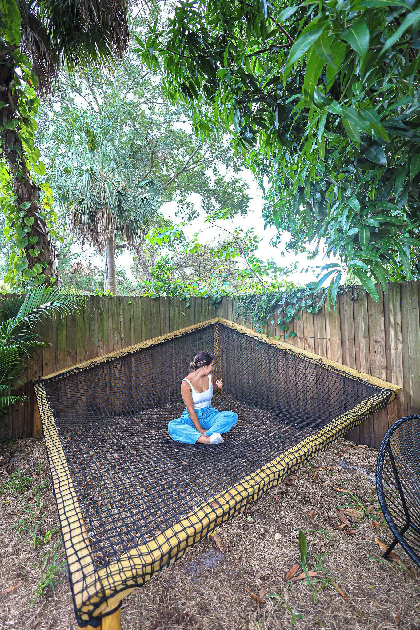 Una hamaca colgada entre dos postes de madera en un jardín con valla de madera y abundante vegetación.
