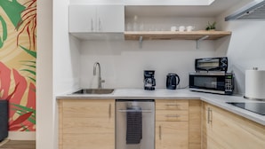 A modern kitchen with a dishwasher, coffee maker, microwave, and a wooden shelf above the sink. - Near Epic Universe & Universal, +parking & Netflix (Orlando)