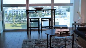 A modern living room with a large window, a round coffee table, and a stack of books on the table. - The Oasis Downtown Fort Myers/Pool View Retreat (Fort Myers)