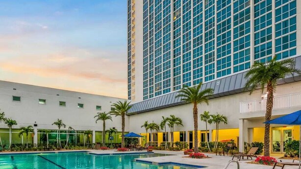 A hotel pool area with a large rectangular pool and a smaller circular hot tub, surrounded by palm trees and lounge chairs. - The Oasis Downtown Fort Myers/Pool View Retreat (Fort Myers)