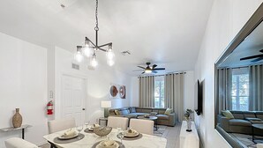 Un coin repas avec une table dressée pour quatre personnes, un canapé et un ventilateur de plafond.