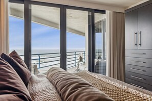 Ein Balkon mit Meerblick, eine Couch mit Kissen, eine Glastür und ein Kleiderschrank mit Schubladen.
