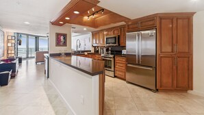 A modern kitchen with wooden cabinets, stainless steel appliances, and a large island. - Ebb Tide - 703 your oceanfront dream vacation destination awaits! (New Smyrna Beach)