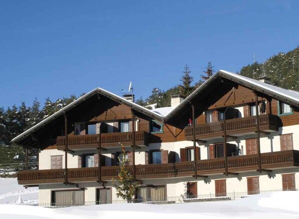 A multi-story building with balconies, a sloped roof, and a snow-covered ground.