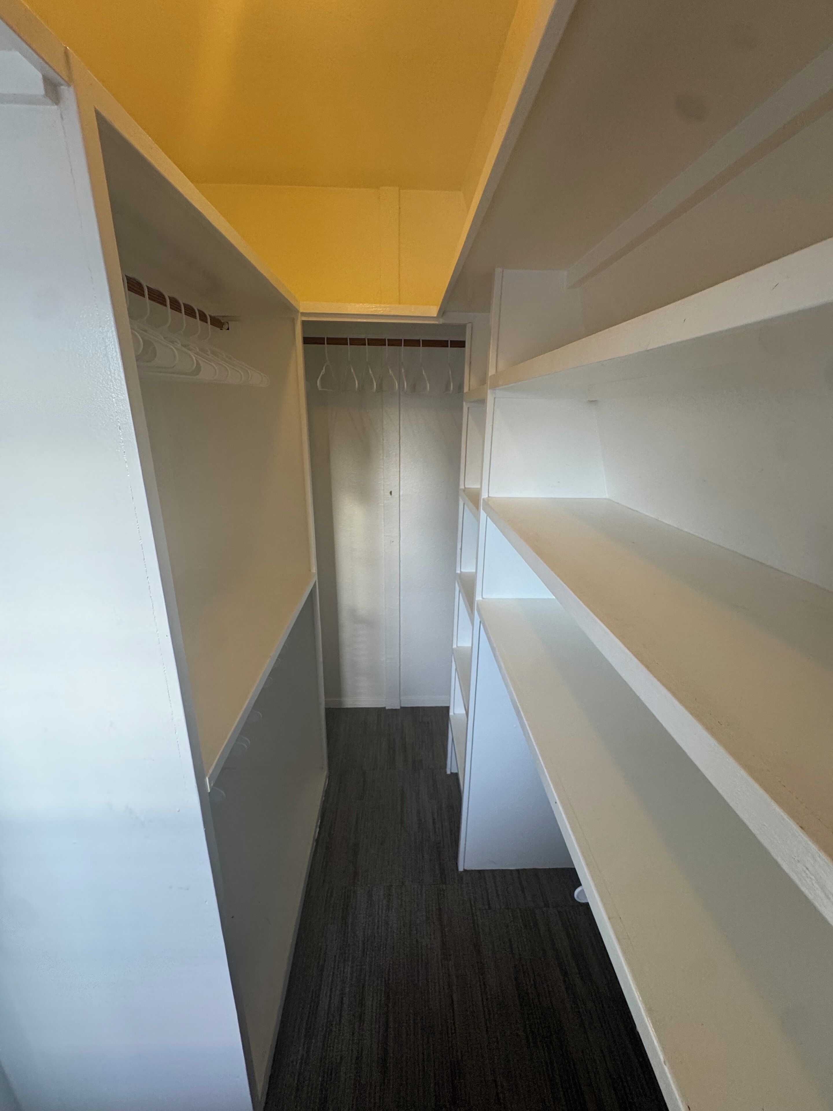 A narrow hallway with white walls and a dark floor, leading to a closet with a hanging rack.