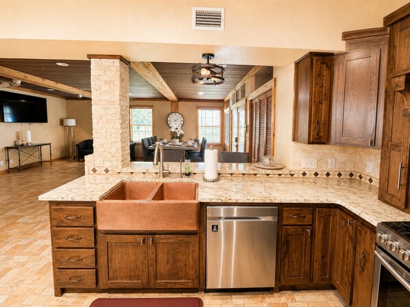 A kitchen with a built-in dishwasher, wooden cabinets, a marble countertop, and a dining area in the background.